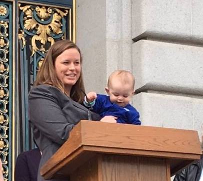 Legal Aid at Work attorney Julia Parish speaking on Paid Family Leave while holding her child at the podium