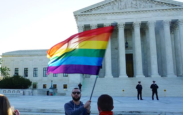 Man holding gay pride flag in front of Supreme Court