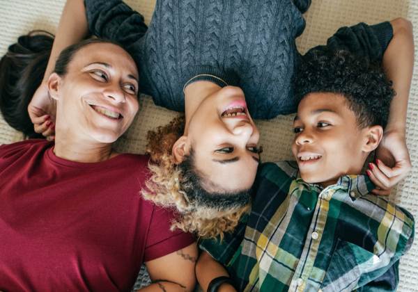 Image of a mother and two children lying on the floor smiling at each other.