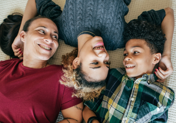 Una madre y dos niños tumbados en el suelo sonriéndose.