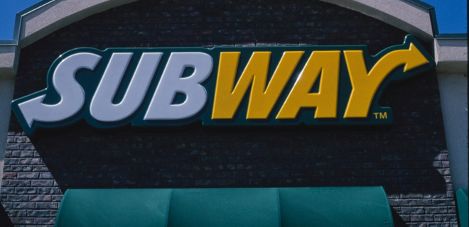Image of Subway logo on a building in white and yellow with a green awning.
